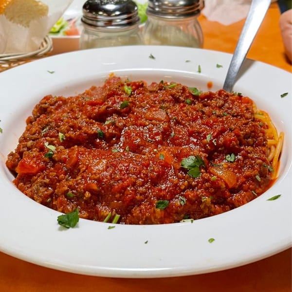 A large white bowl of spaghetti with rich red meat sauce and fresh parsley, with a spoon.