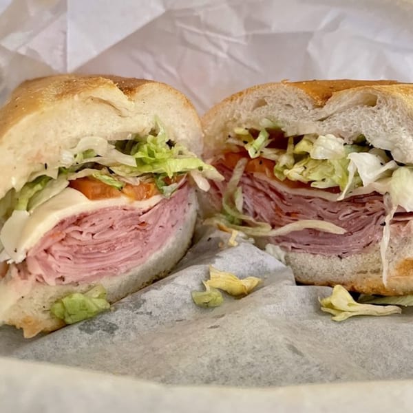 A large Aljon's Grill Pizzeria & Restaurant sub sandwich, cut in half, filled with meat, cheese, and vegetables.