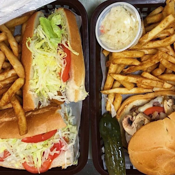 Two baskets of Aljon's Grill Pizzeria & Restaurant subs with fries, coleslaw, and a pickle.